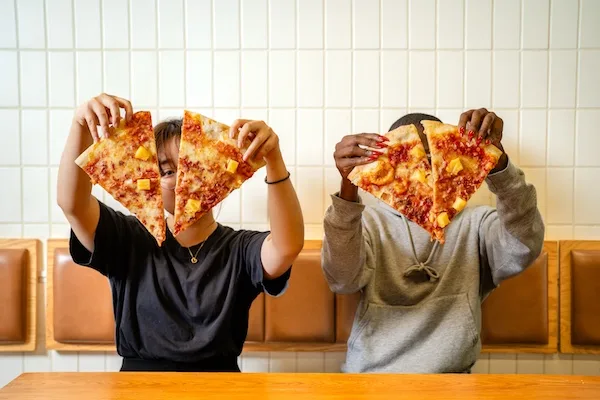 Photo of two people holding up slices of pizza, made at Wiseguy, a Thompson Restaurant location that accepts meal swipes.